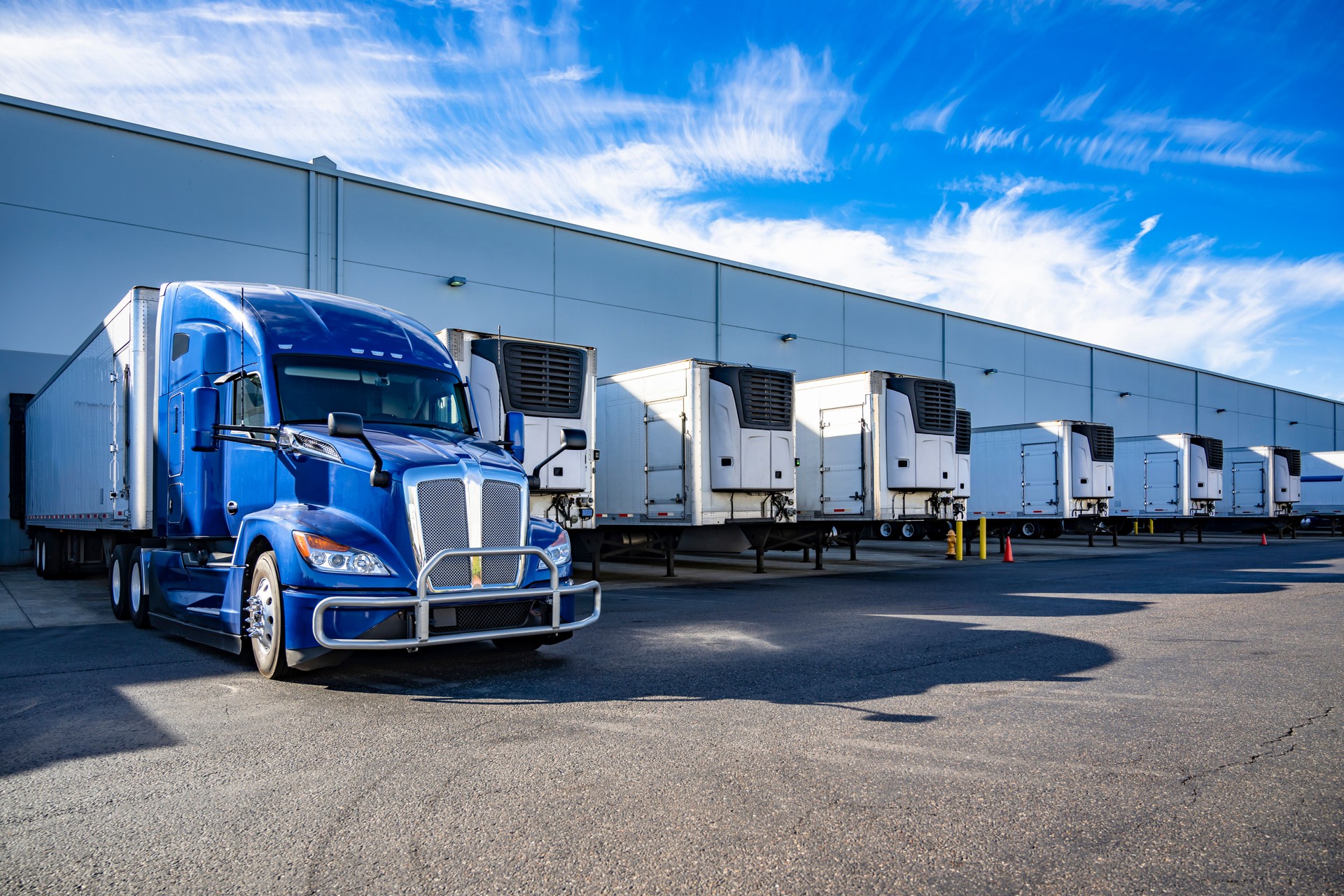 Big rig blue semi truck with refrigerator semi trailer standing in row with another semi trailers in warehouse dock gates loading cargo for the next freight